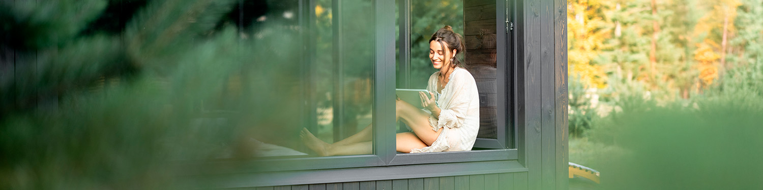 Frau mit Tablet sitzt am Fenster – Blick aus dem Garten – Banner zum Beitrag "Was passiert mit meinen Umfrageantworten?"