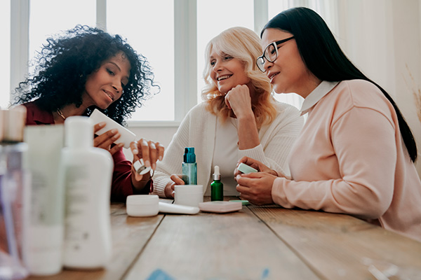 Drei Frauen sitzen nebeneinander am Tisch und sehen sich Kosmetikprodukte an – Marktforschungsmethoden in Online-Panels