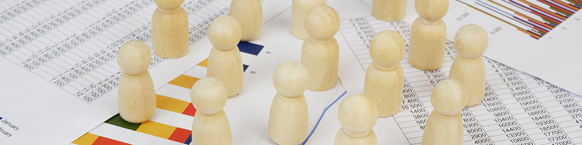 Titelbild – Papier bedruckt mit Zahlentabellen und Statistiken bedecken den Tisch, darauf einige hölzerne Spielfiguren – symbolischer Banner zu Profilumfragen in Marktforschungspanels