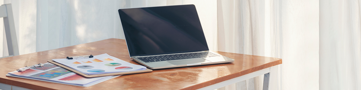 Tisch mit zwei Klemmbrettern mit Papierbögen voller Statistiken und Graphen zum Thema Onlinebevölkerung. Daneben ein ausgeschalteter aufgeklappter Laptop.