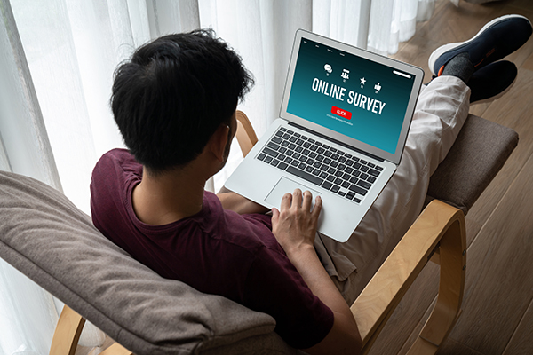 Blick über die Schulter einer Person mit Laptop auf dem Schoß - die Benchmark-Fragen in Online-Umfragen ausfüllt